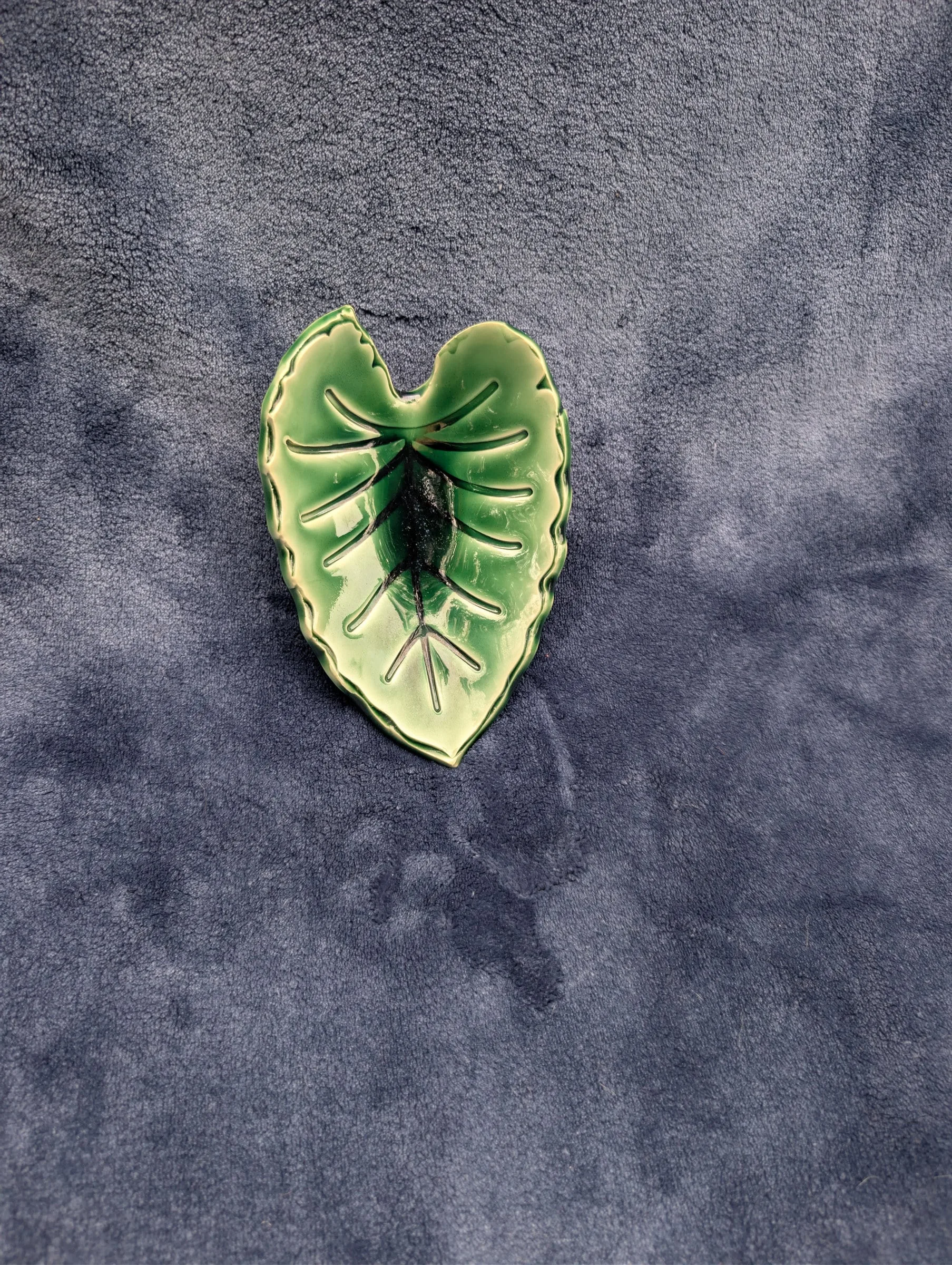 A small, glossy bright-green dish shaped like a broad leaf, with a dark patch at the center and a raised edge and veins.