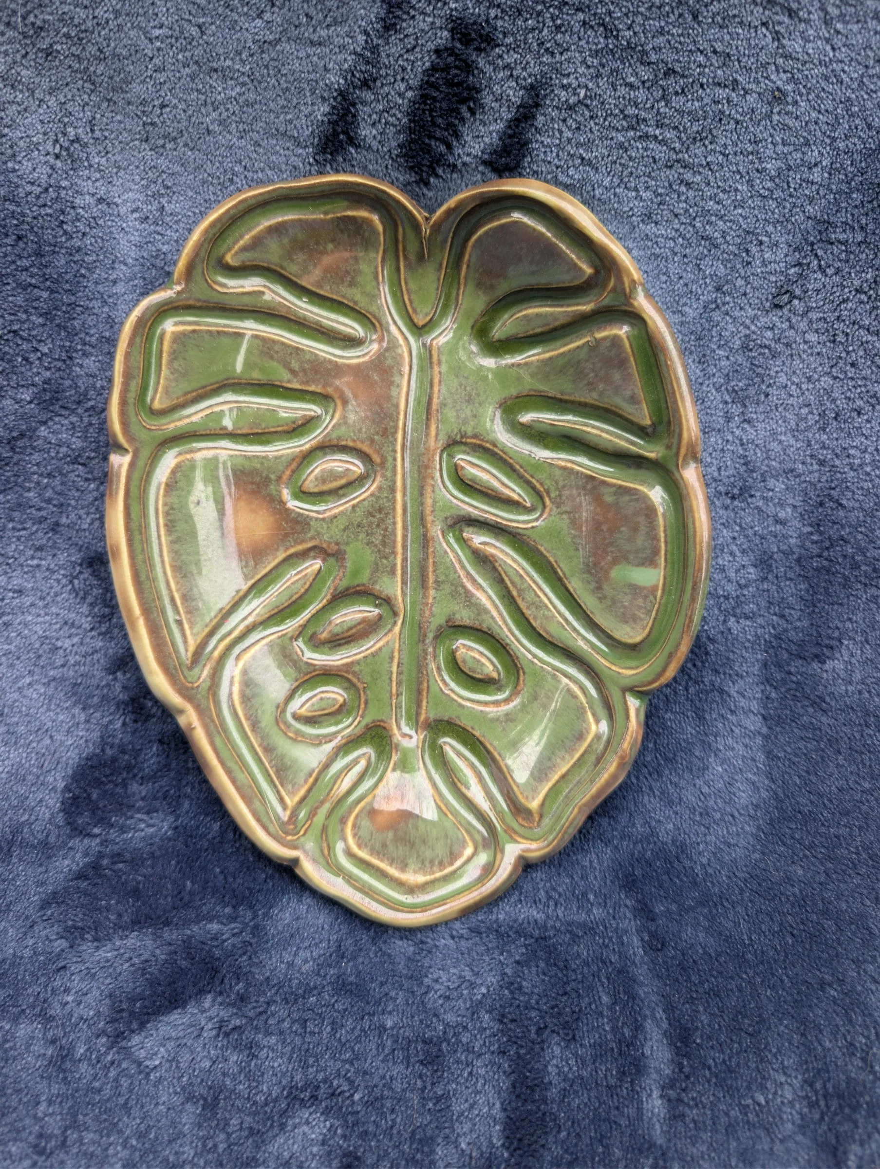 A leaf-shaped plate with several cut-out windows, glazed green with a raised gold-toned rim and outlined veins.