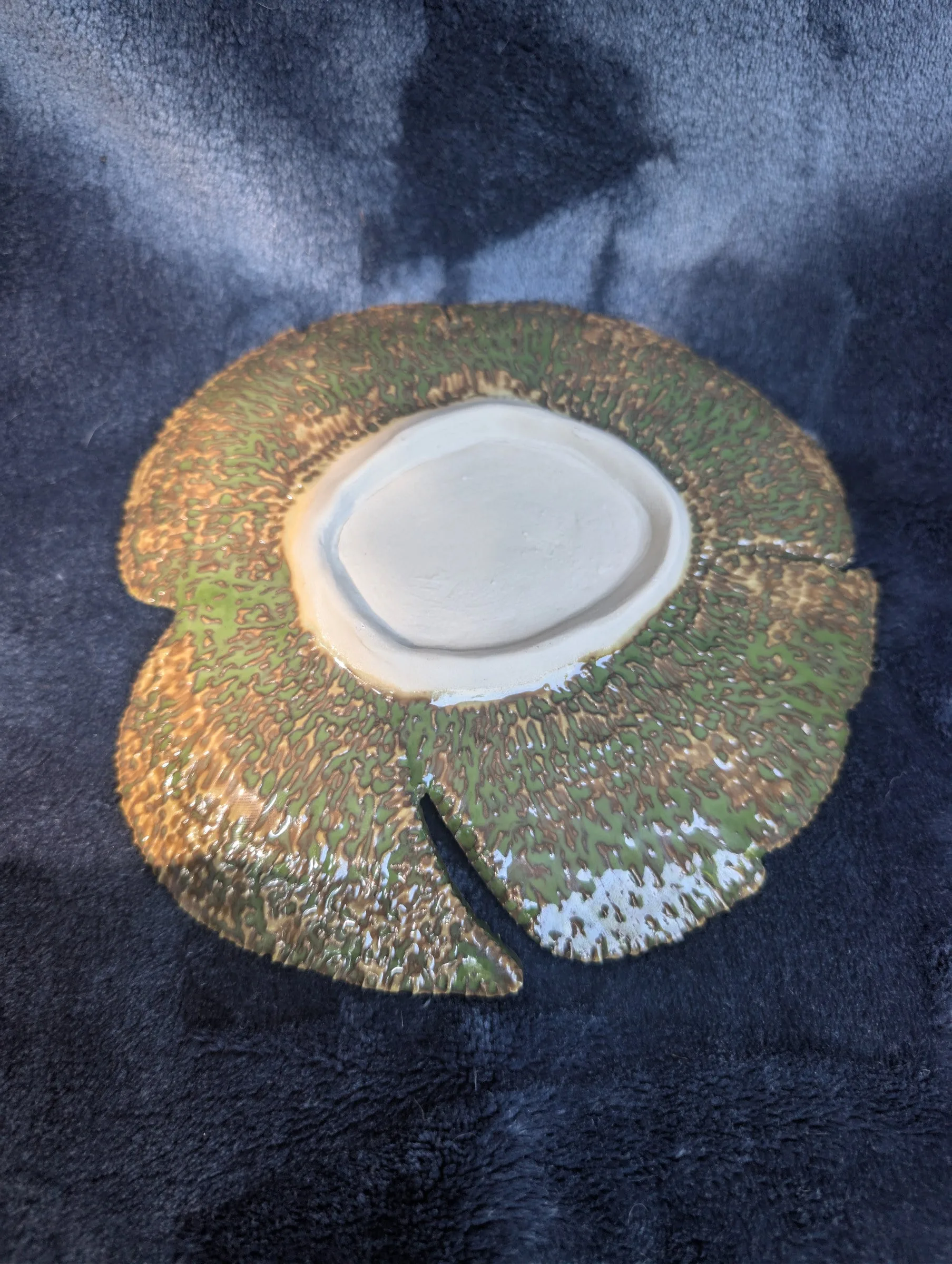 A large round plate with a speckled green and gold outer rim, a plain glossy rim and a white well, with one notch cut into the edge at the right.