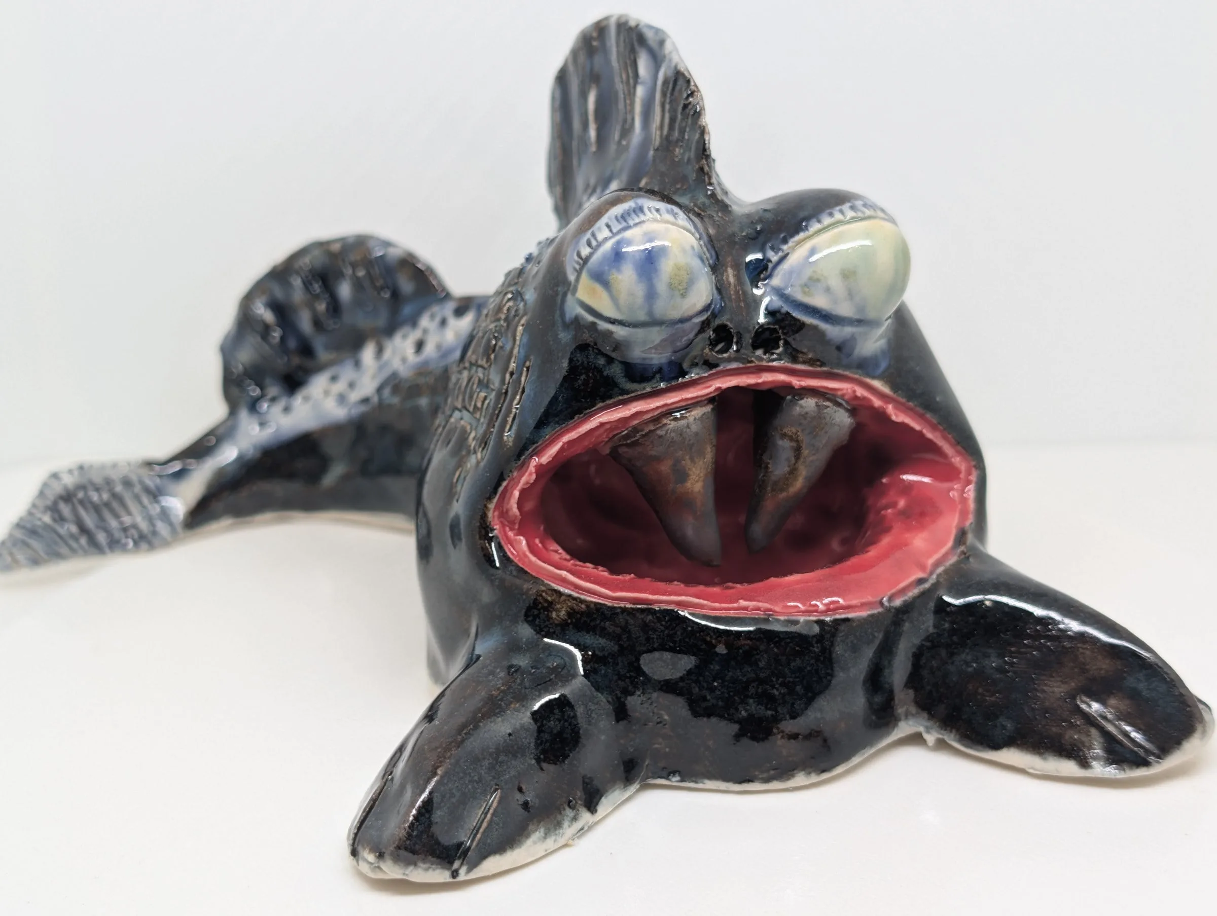 A glossy black glazed creature with a wide open red mouth, pale blue-white eyes and a scaled ridge running down its back.