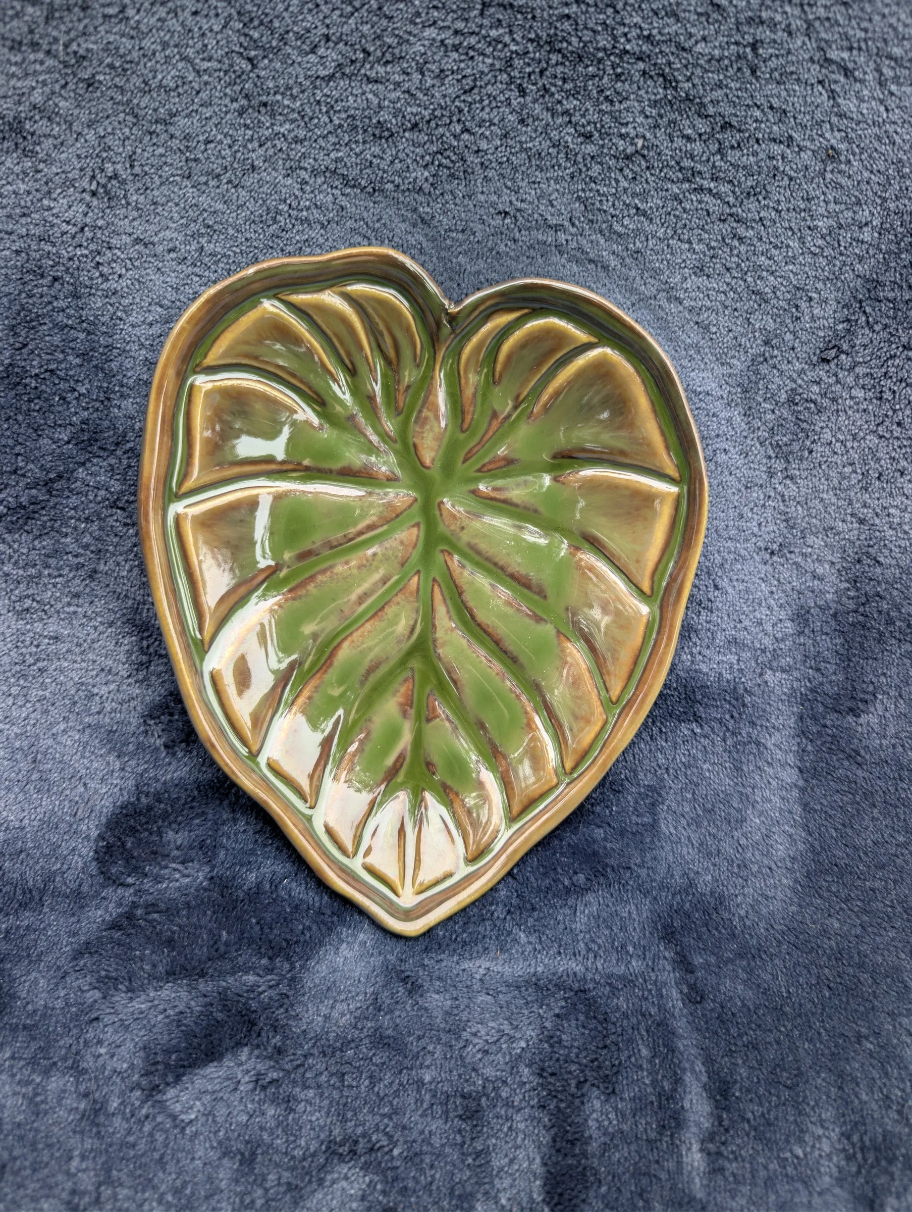 A second heart-shaped leaf dish in olive green and amber, its veins raised above the surface of the glaze.