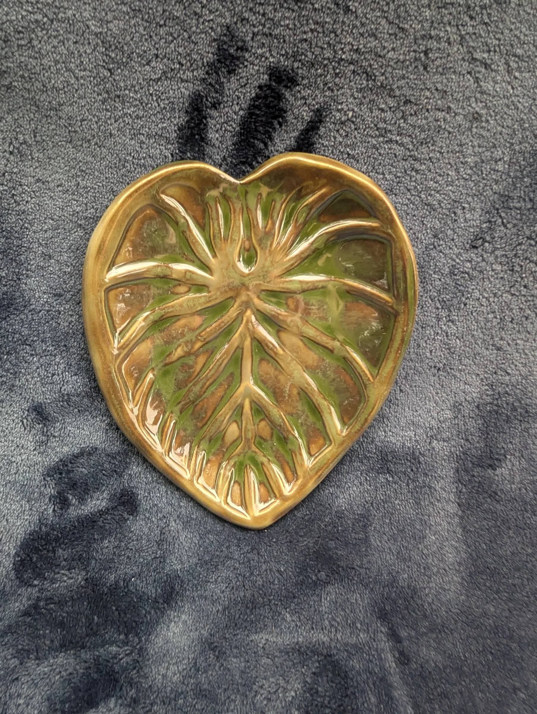 A heart-shaped leaf dish with a green center and a gold-toned rim, lit so the glaze reads almost metallic.